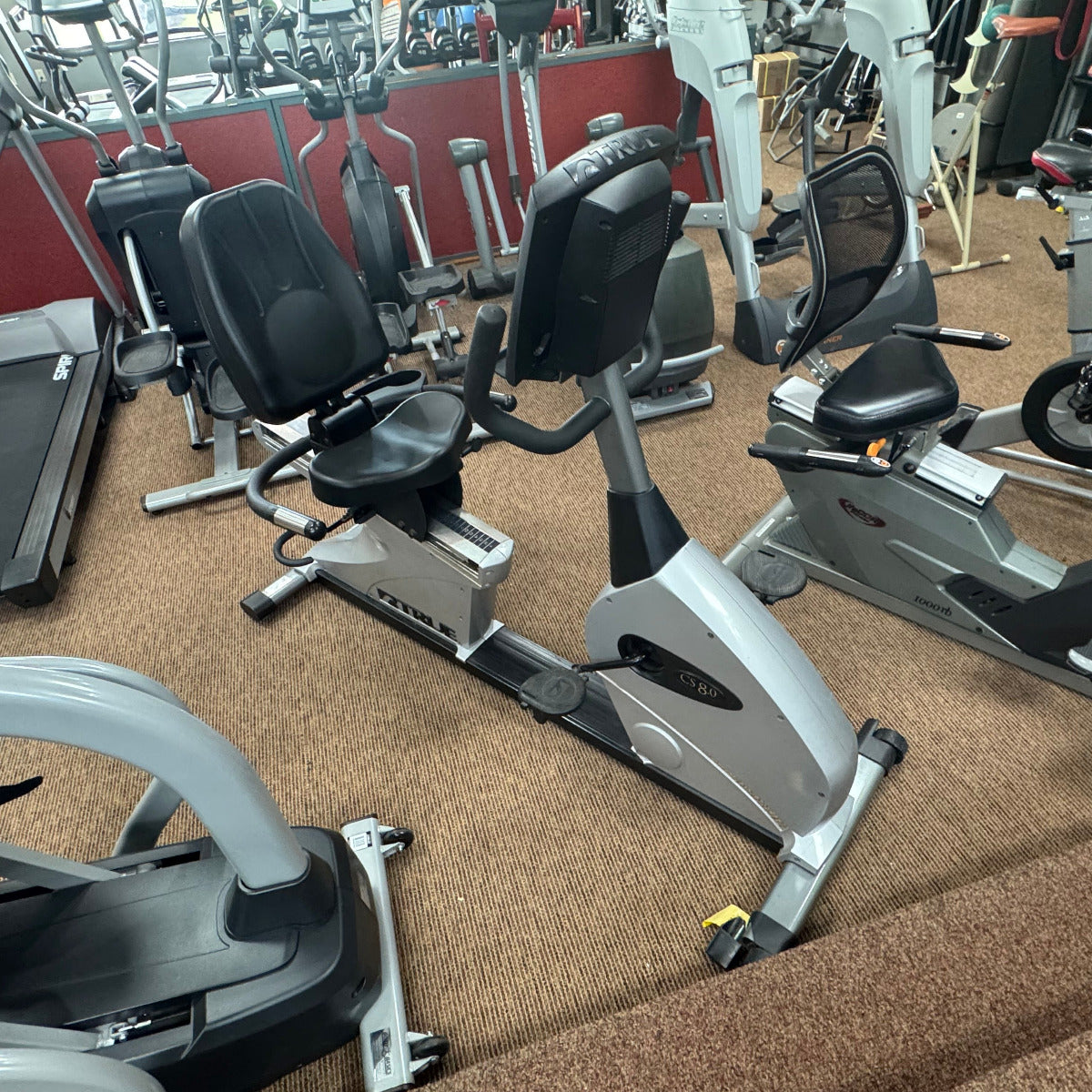 Gym equipment including treadmills and stationary bikes on a carpeted floor.