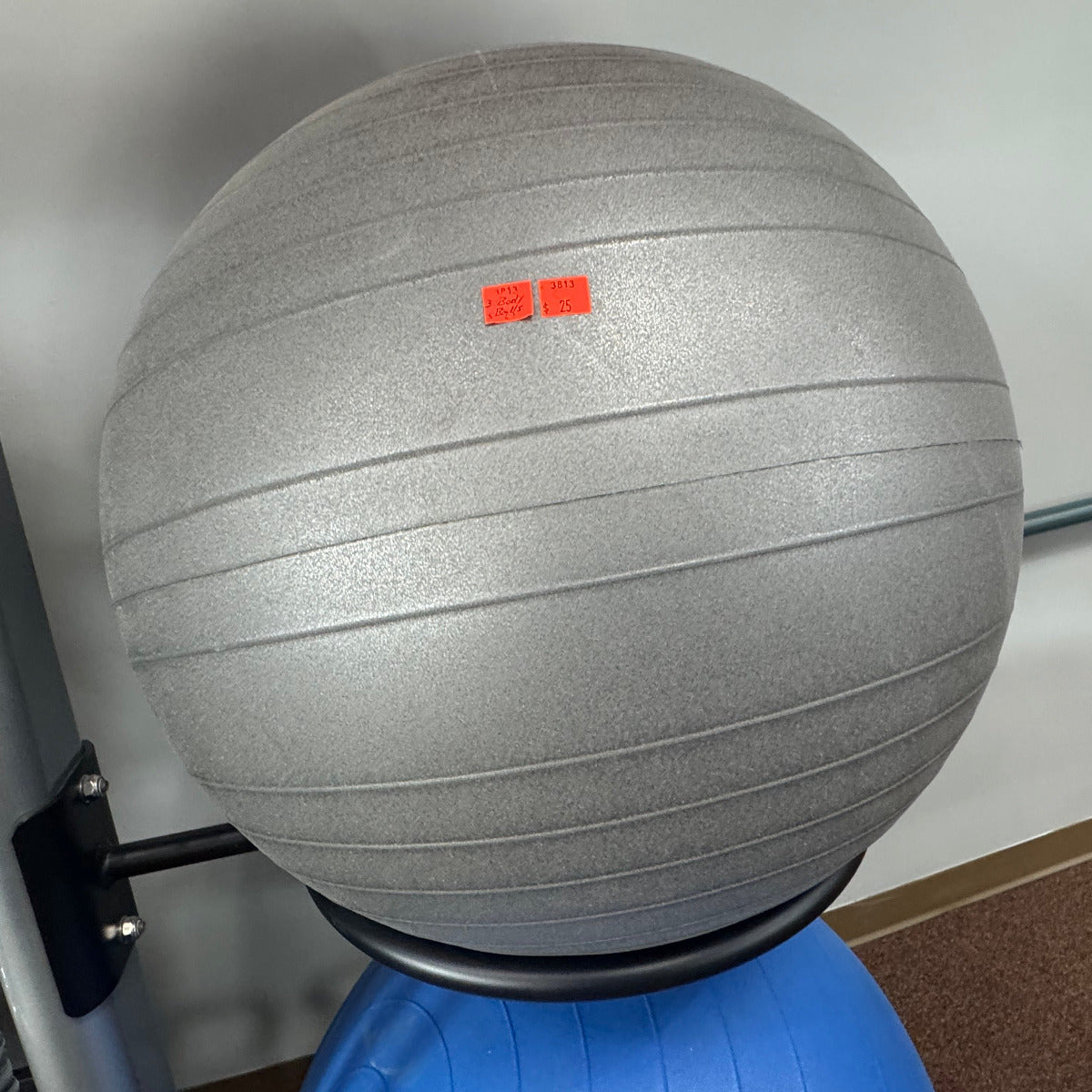 Gray exercise ball with a red logo on a blue base against a white wall.