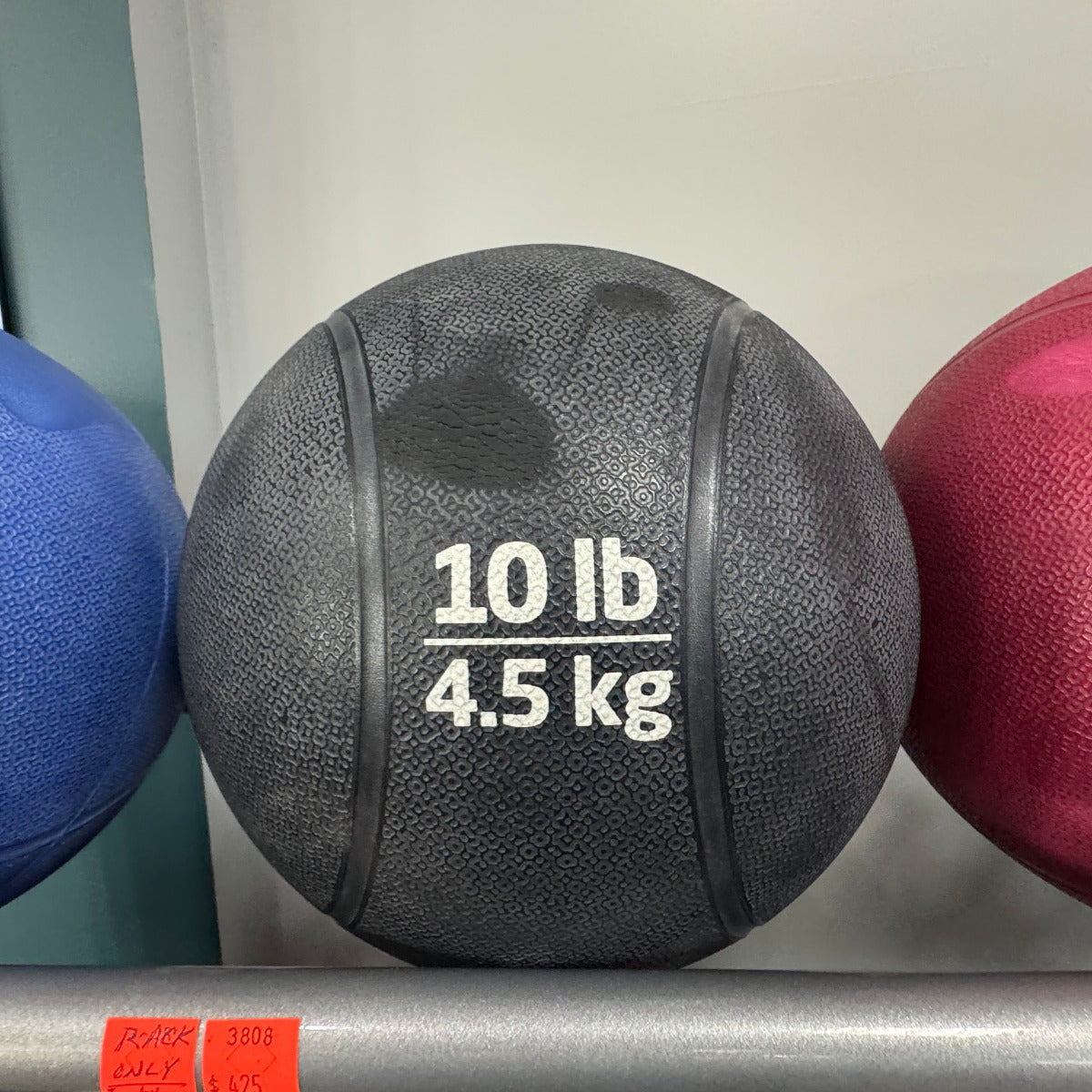 Black medicine ball labeled '10 lb 4.5 kg' on a rack with other balls.