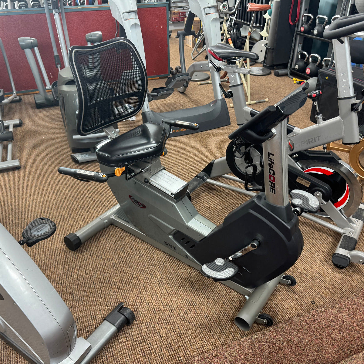 Gym interior with various exercise bikes and equipment on a carpeted floor.
