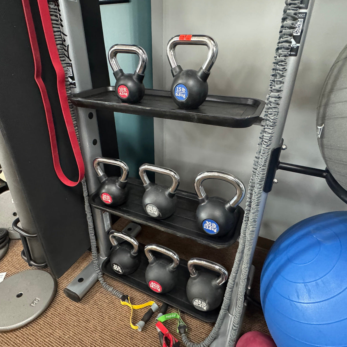 Set of kettlebells on a rack in a gym setting with exercise ball and equipment.