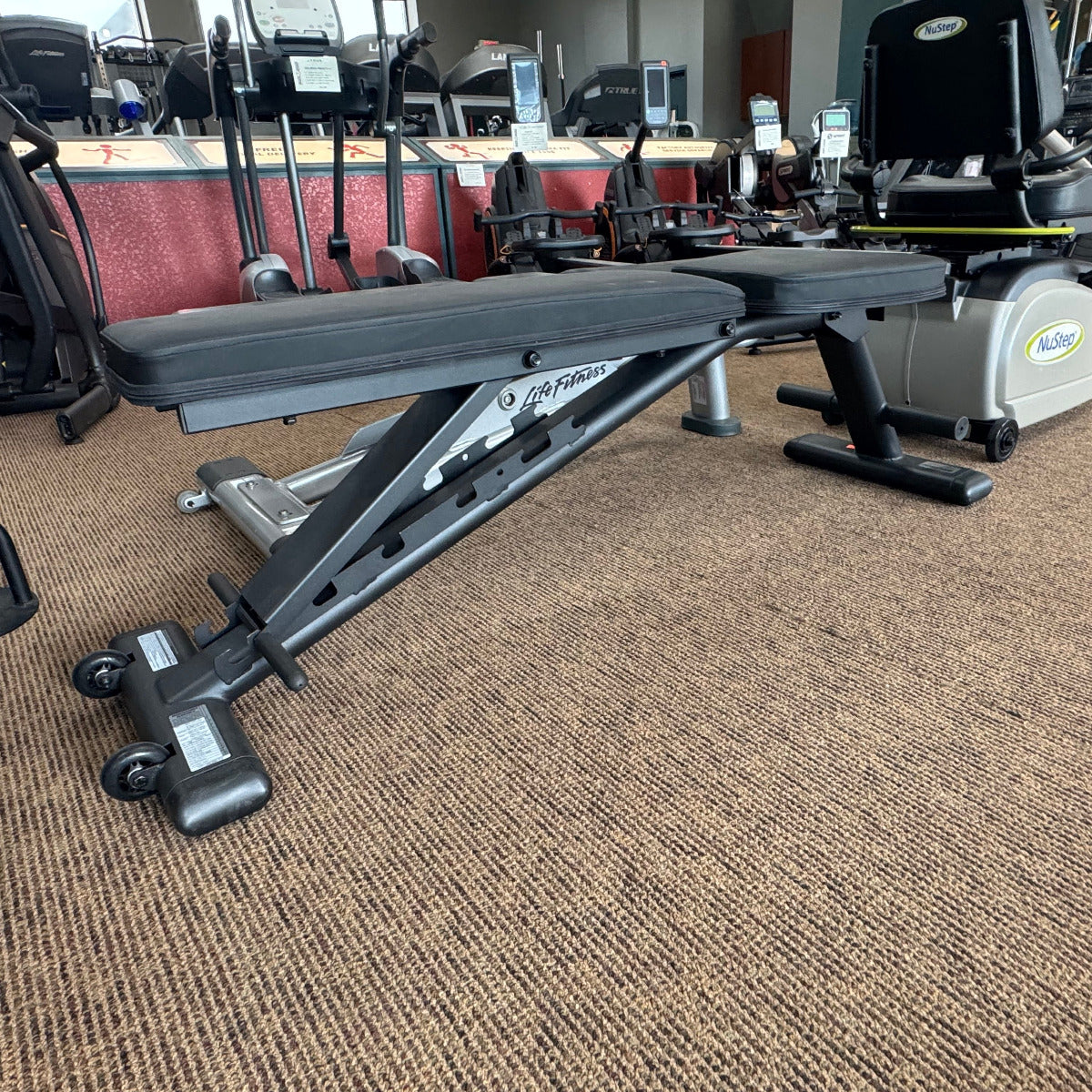 Gym equipment including a weight bench and cardio machines on a carpeted floor.