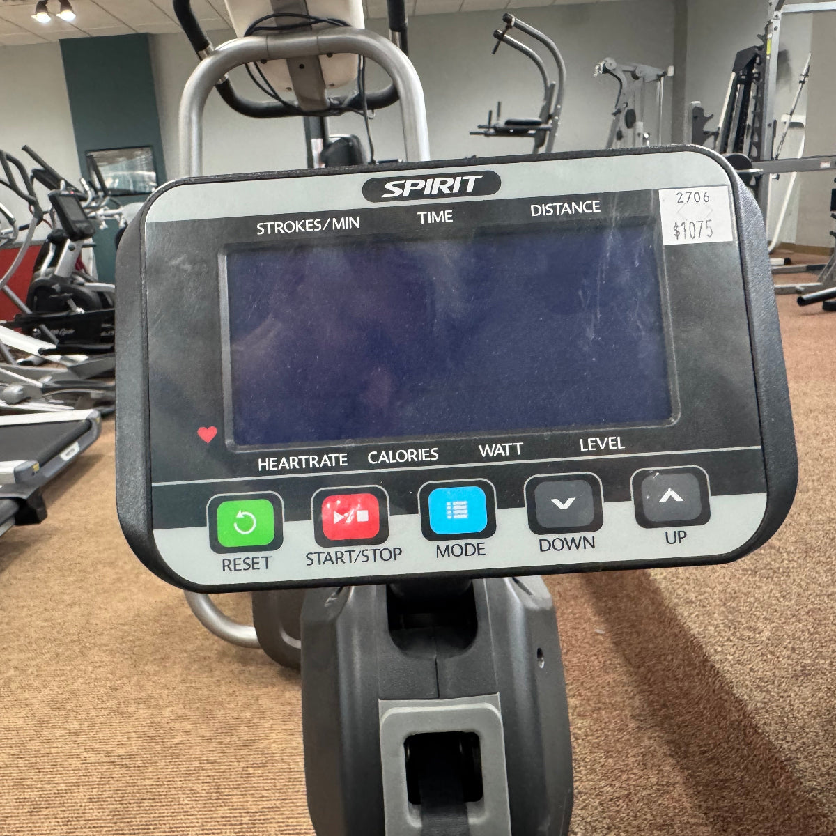 A close-up of a Spirit brand cardio machine console in a gym setting, showing the screen and buttons including reset, start/stop, mode, down, and up.