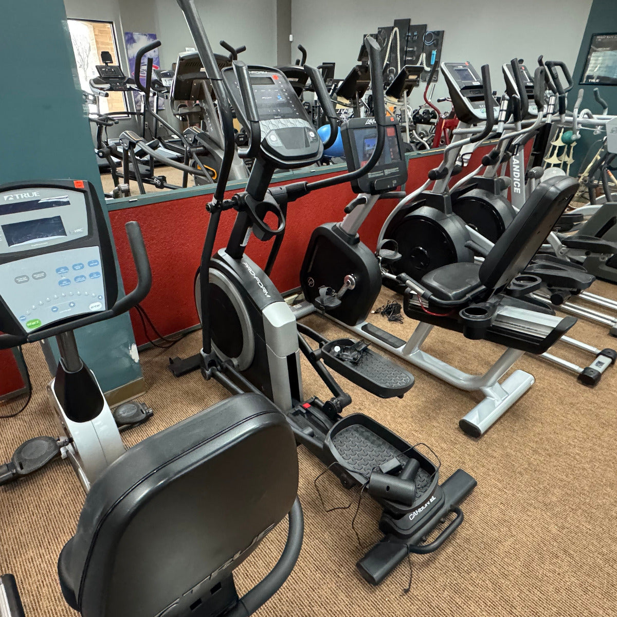 Gym interior with elliptical machines and treadmills on a carpeted floor.
