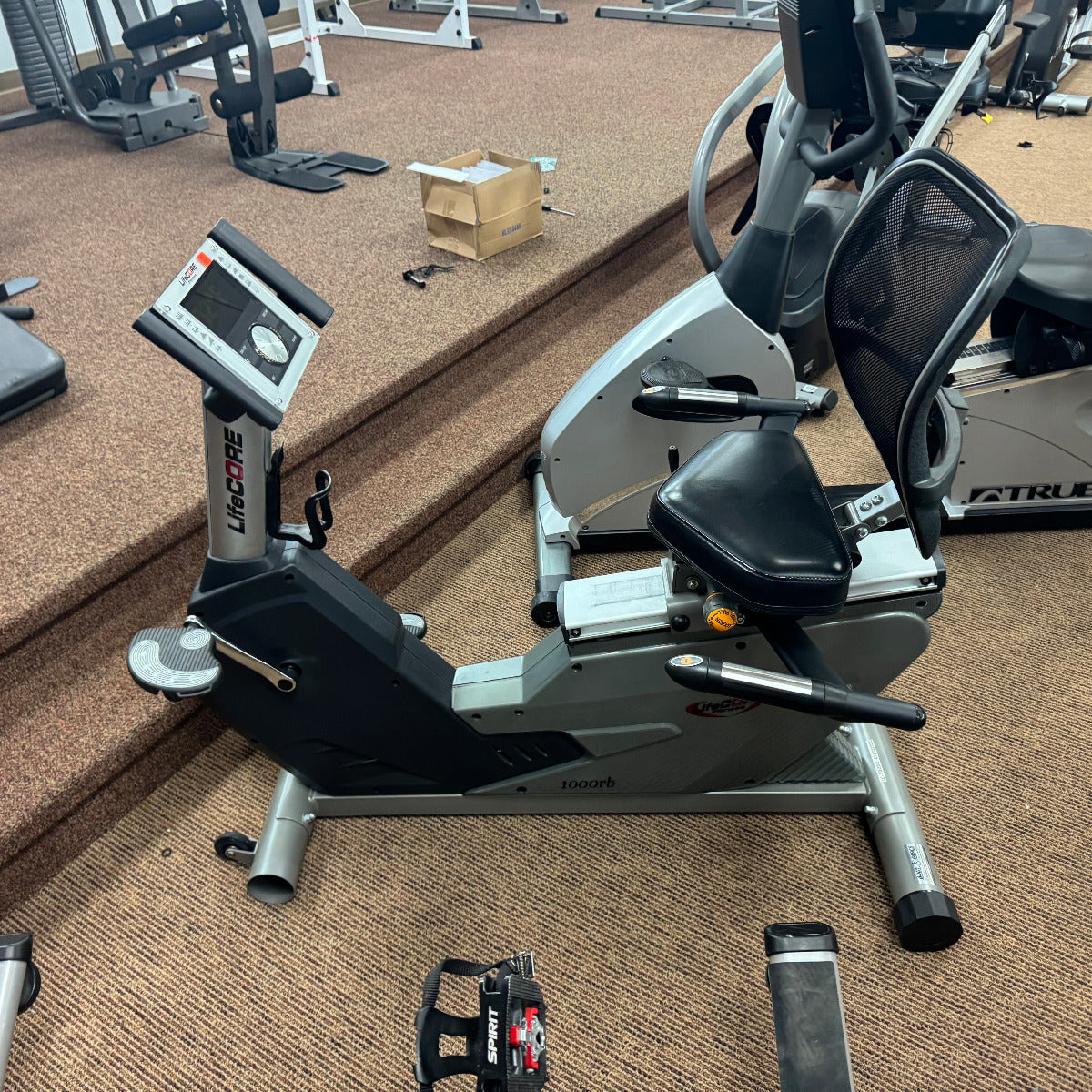 Recumbent bike in a gym setting with equipment scattered around