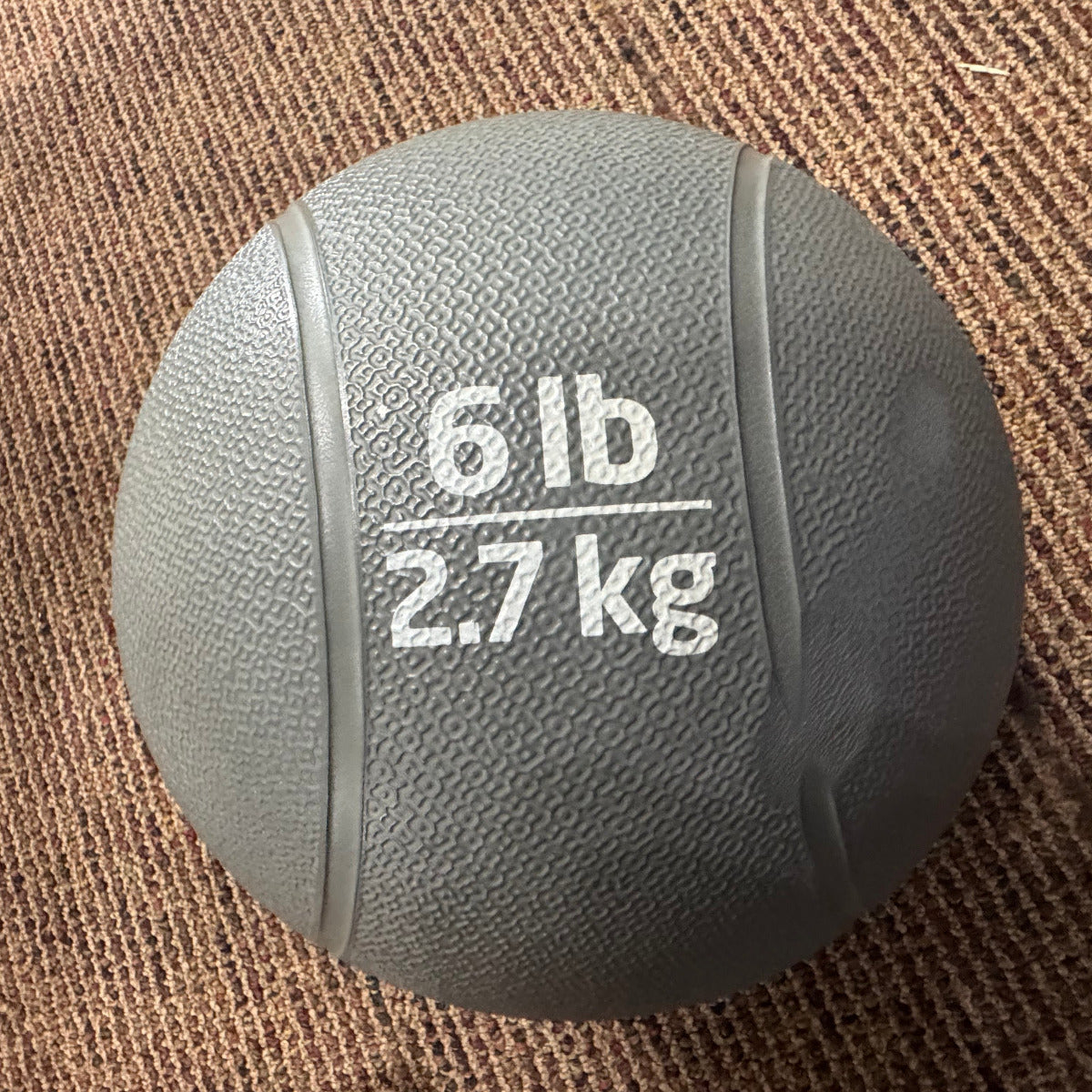 Gray medicine ball labeled '6 lb 2.7 kg' on a brown textured surface