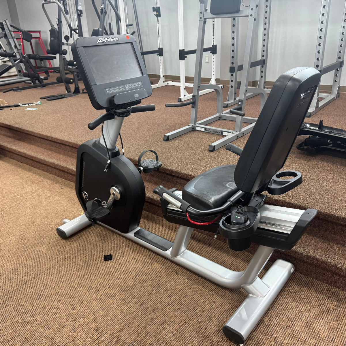 Recumbent bike in a gym setting with various equipment in the background