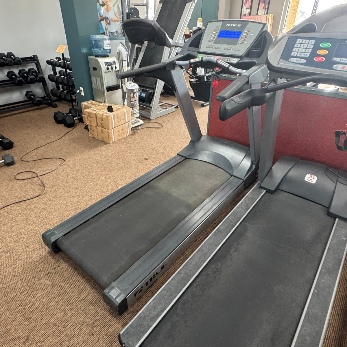 Treadmills in a gym setting with various equipment in the background