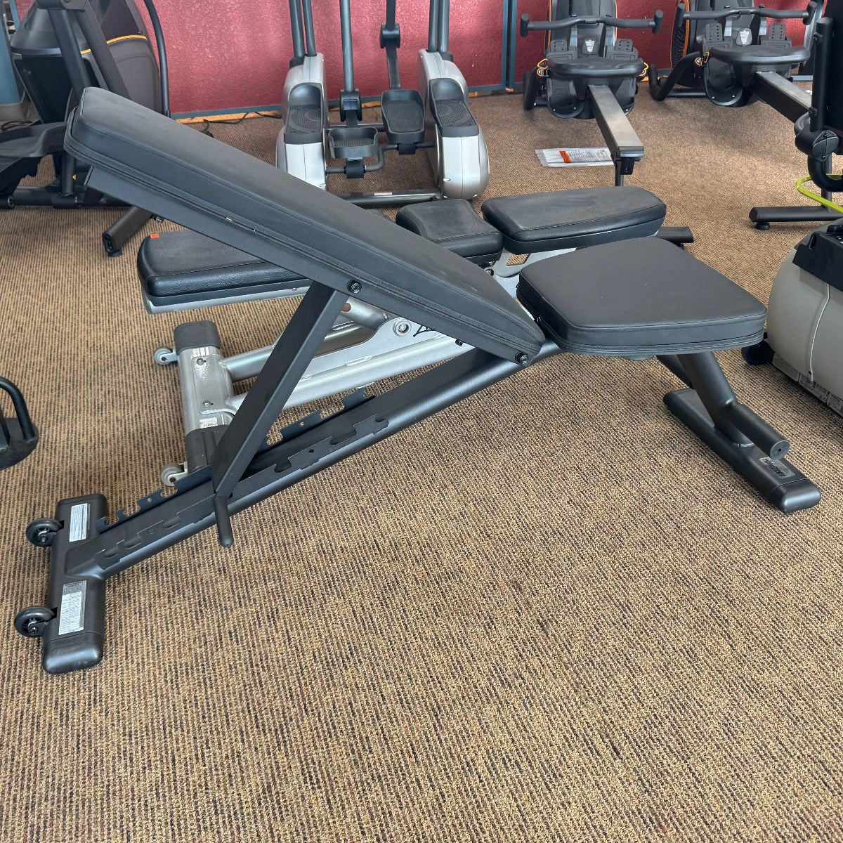 Gym bench in a gym setting with various equipment in the background
